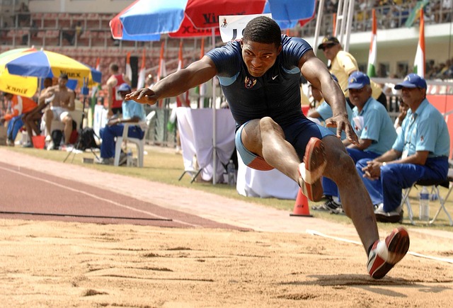 A male athlete in the air as he jumps at the long jump pit